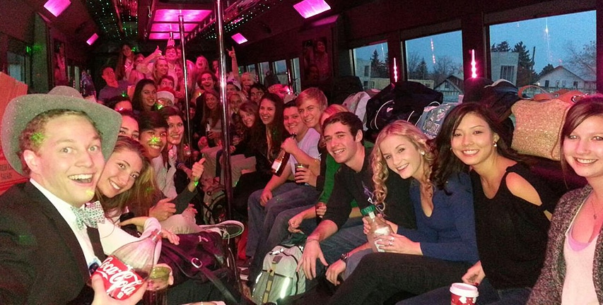 A photo inside of one of our party bus, filled with happy, smiling people. Many drinks, and a whole crowd at the end of the bus.