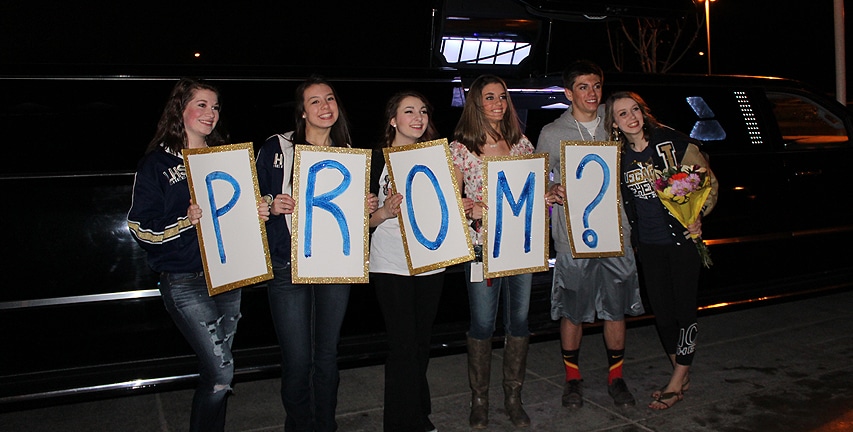 Multiple people holding up signs that spell out Prom?